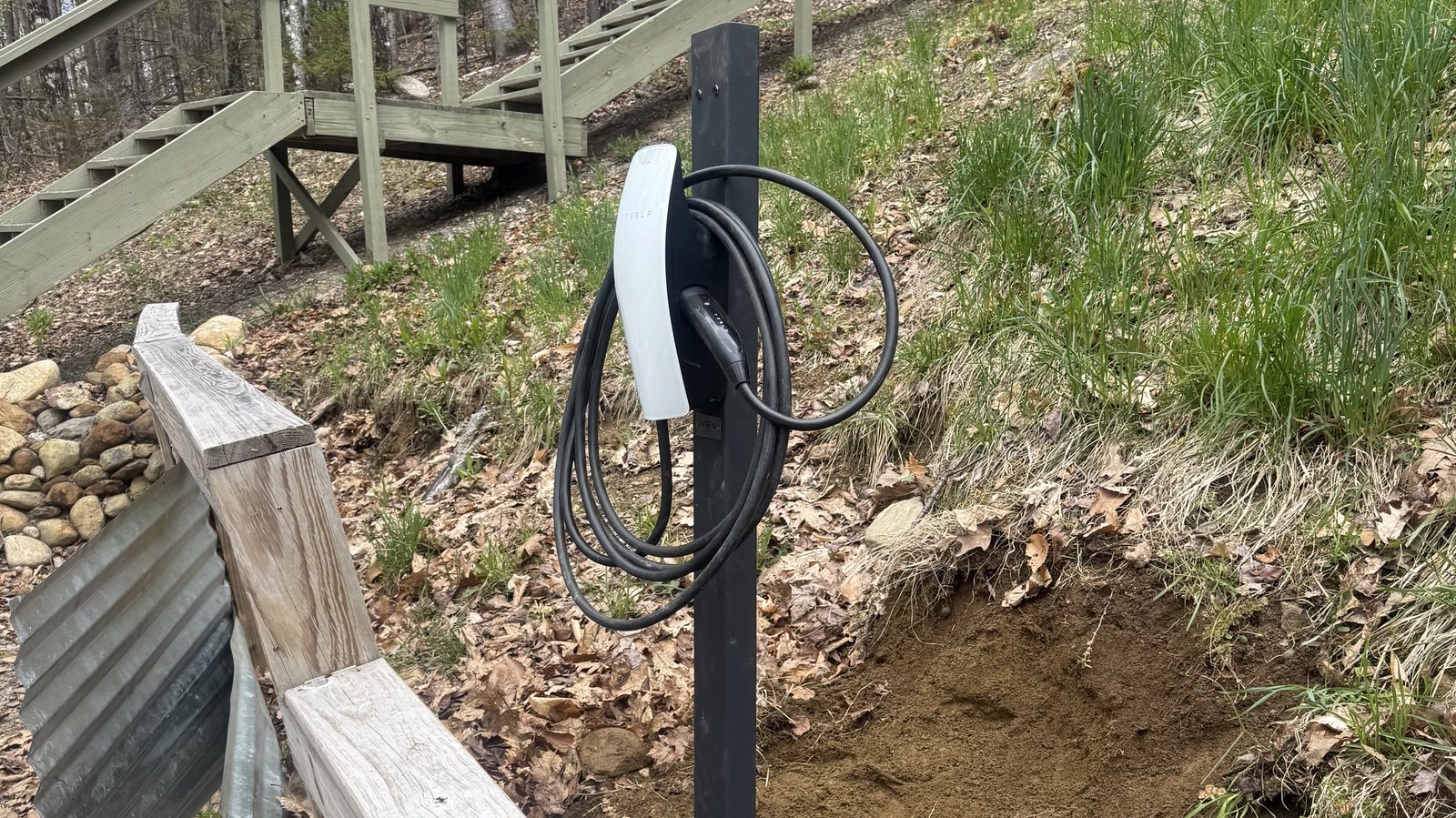 Tesla wall connector on a pedestal post on a wooded hillside lot