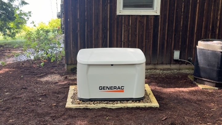 Generac standby generator on a pad beside a stained-cedar lakeside home